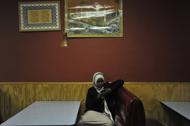 Hamdi texts her friends while waiting in the Quruxlow restaurant in Minneapolis, in 2011. An image of Mecca, and verses from the Quran hang in the background. Hamdi's poetry often mentions her strong faith in God.